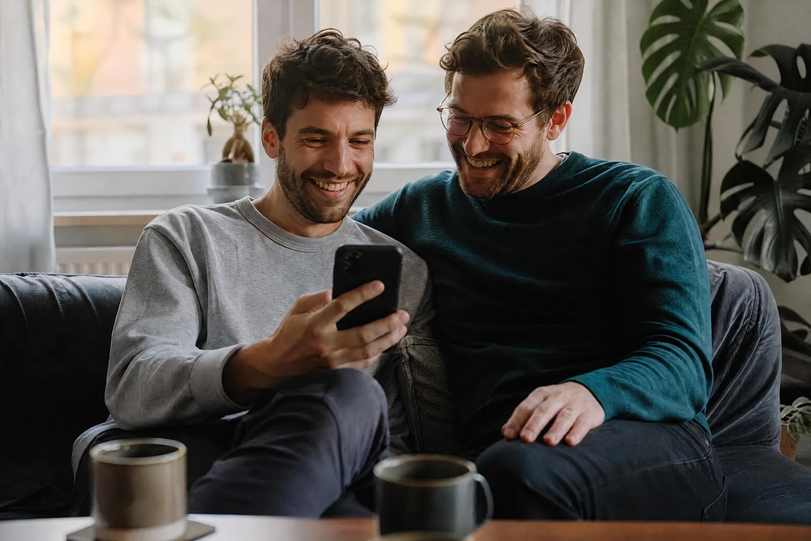Zwei Freunde sehen sich auf dem Sofa gemeinsam eine Einladung am Handy an
