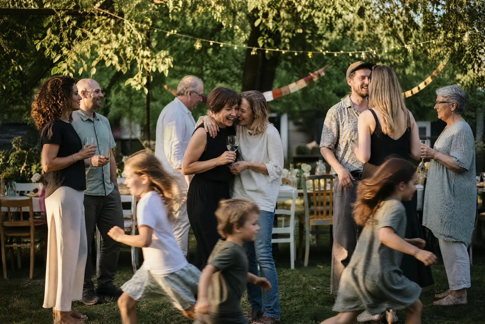 Gartenfest zum vierzigsten Geburtstag, Erwachsene mit Gläsern, Kinder rennen vorbei