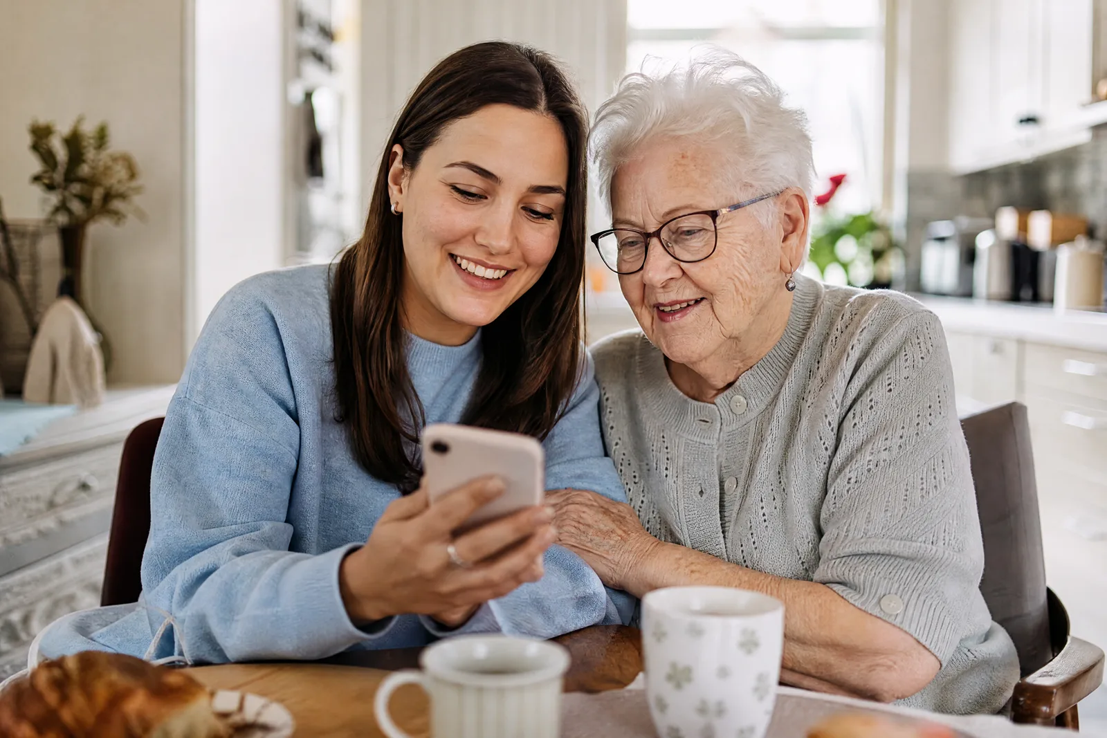 Eine junge Frau liest ihrer Grossmutter eine Einladung vom Handy vor