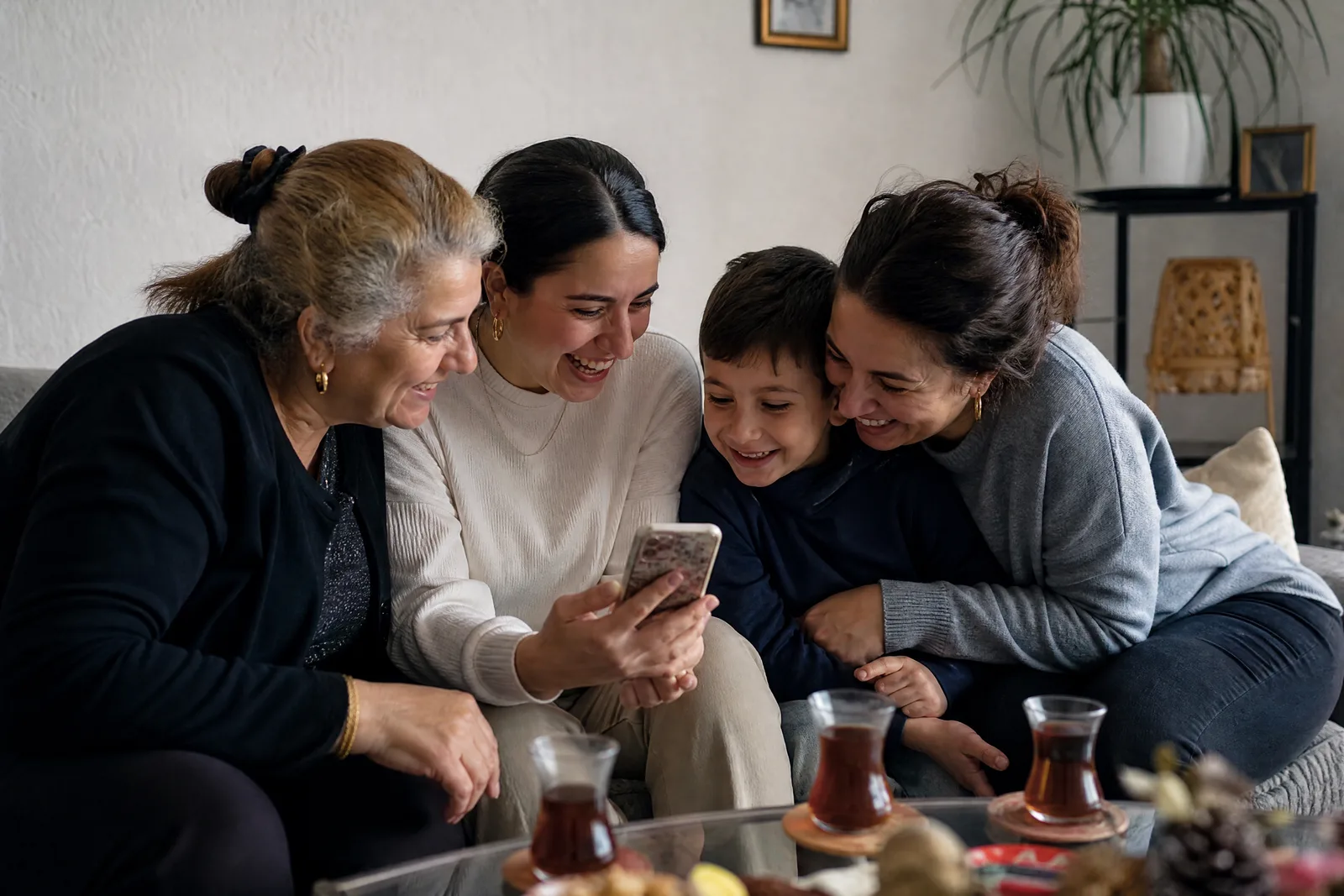 Eine türkisch-deutsche Familie sieht sich im Wohnzimmer gemeinsam eine Einladung auf dem Handy an