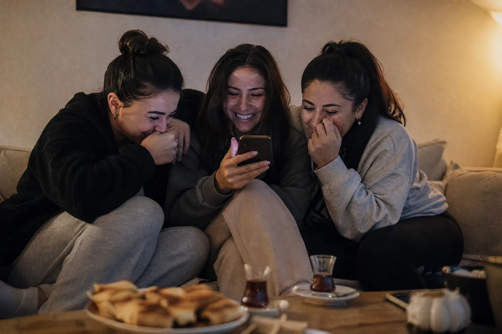 Drei junge Frauen sehen sich auf dem Sofa gemeinsam eine Einladung am Handy an