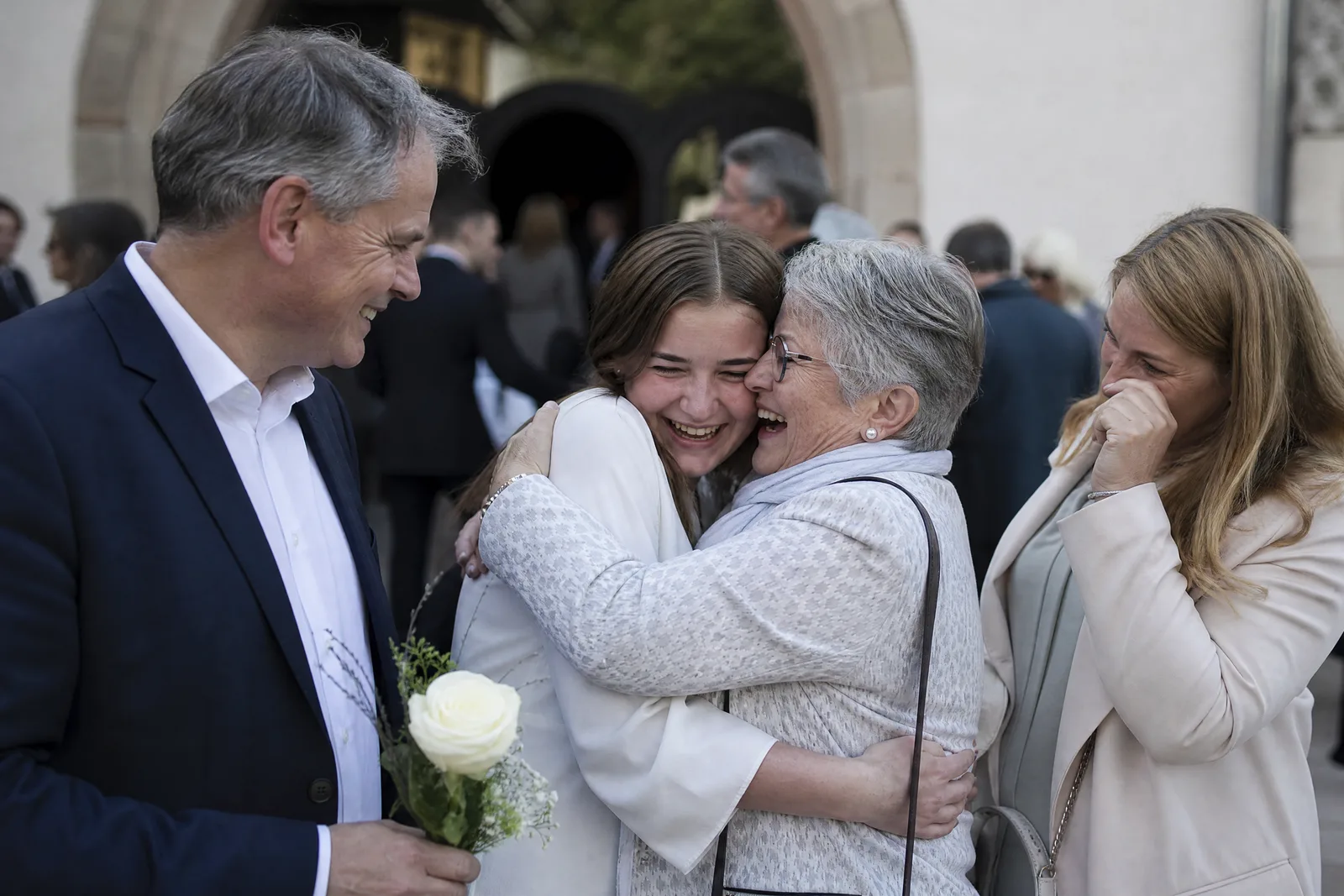 Eine Konfirmandin wird nach dem Gottesdienst von ihrer Grossmutter umarmt, die Eltern stehen daneben