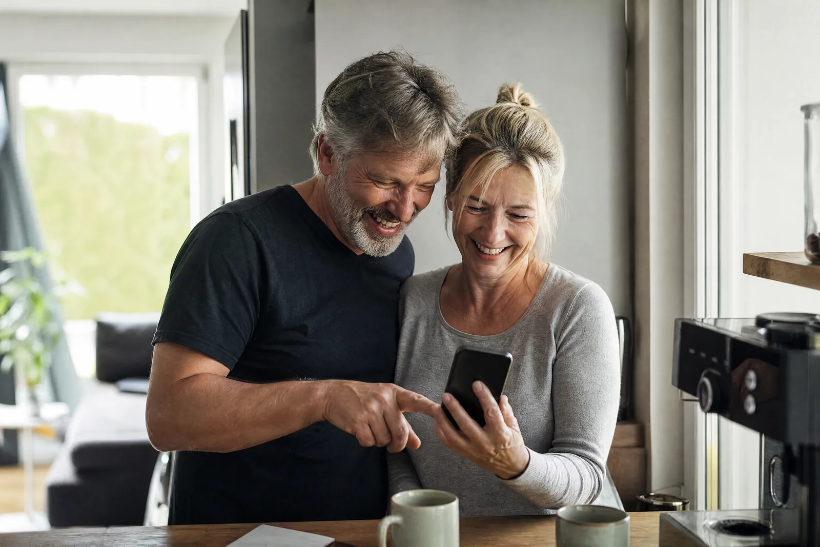 Ein Paar sieht sich in der Küche gemeinsam eine Einladung am Handy an