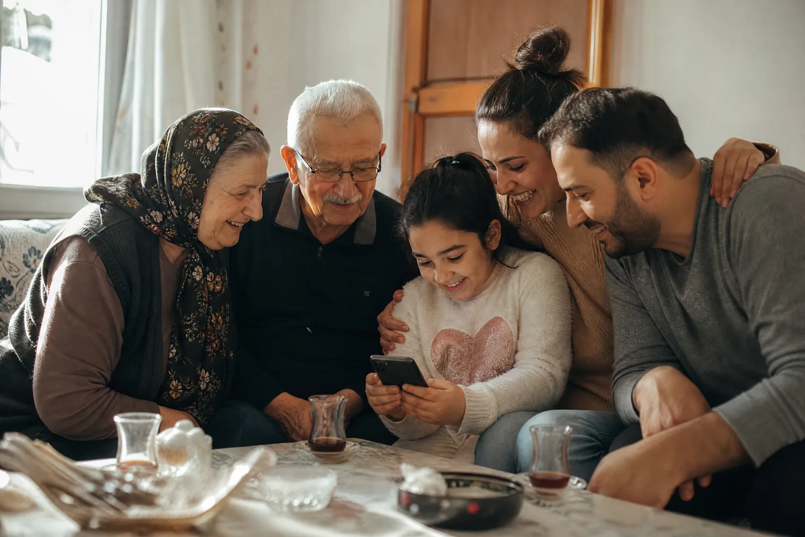 Drei Generationen einer türkisch-deutschen Familie sehen sich bei Tee eine Einladung am Handy an