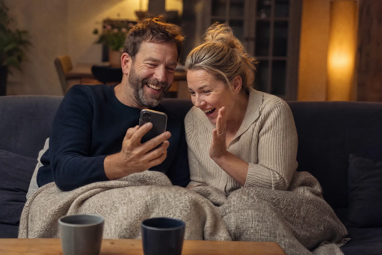 Ein Paar auf dem Sofa zeigt sich gegenseitig lachend etwas auf dem Handy