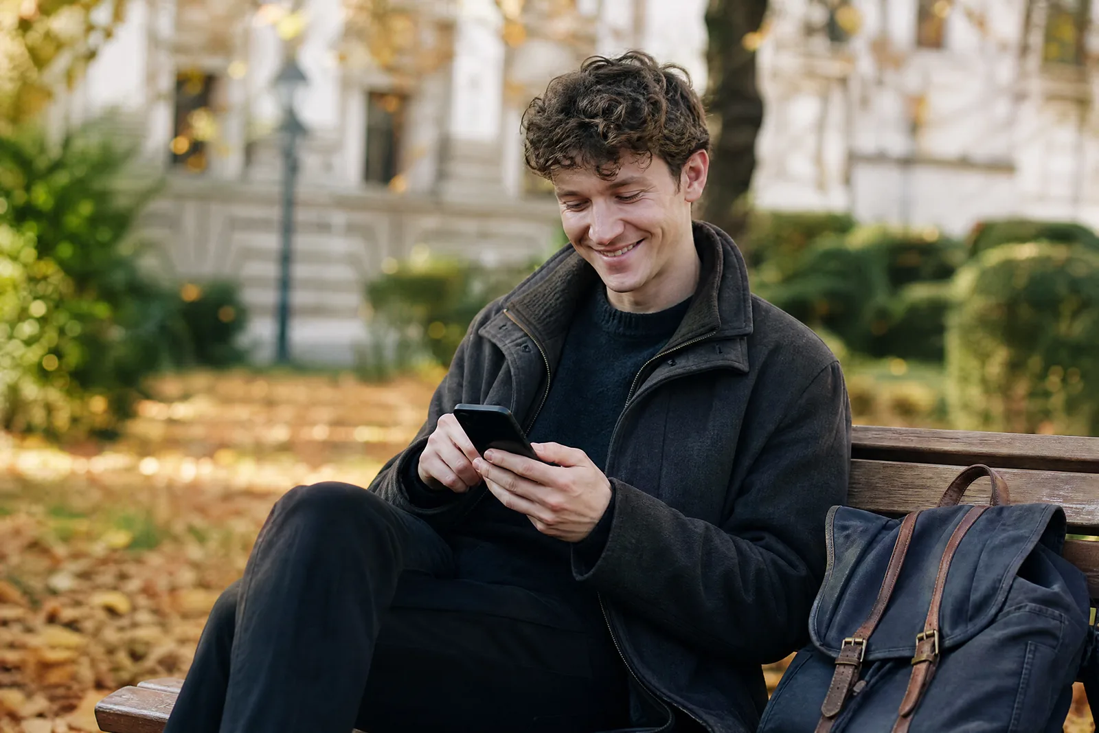 Ein junger Mann sagt auf einer Parkbank mit dem Daumen auf dem Handy zu